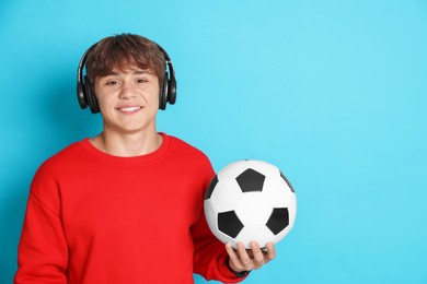 Photo of Portrait of smiling teenage boy in headphones with soccer ball on light blue background. Space for text