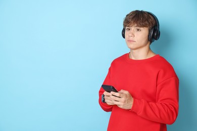 Photo of Cute teenage boy in headphones with smartphone on light blue background. Space for text