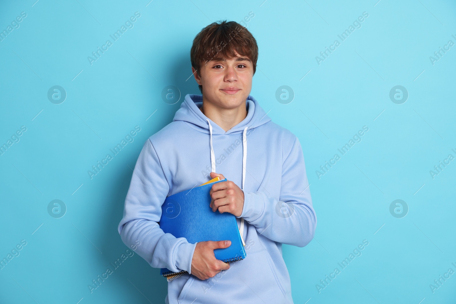 Photo of Portrait of cute teenage boy with book on light blue background