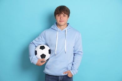 Photo of Portrait of cute teenage boy with soccer ball on light blue background