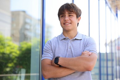 Photo of Smiling teenage boy with crossed arms near building outdoors, low angle view