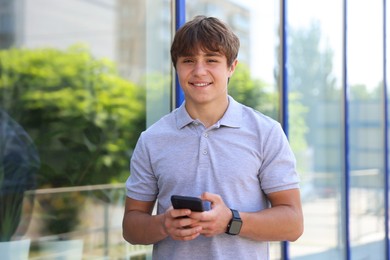 Photo of Portrait of smiling teenage boy with smartphone near building outdoors