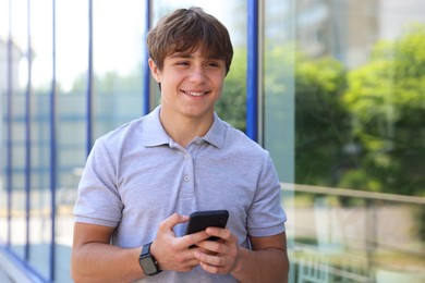 Photo of Smiling teenage boy with smartphone near building outdoors