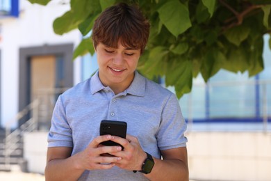 Photo of Smiling teenage boy with smartphone on city street