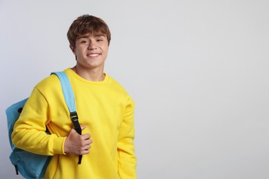 Photo of Portrait of smiling teenage boy with backpack on light grey background. Space for text