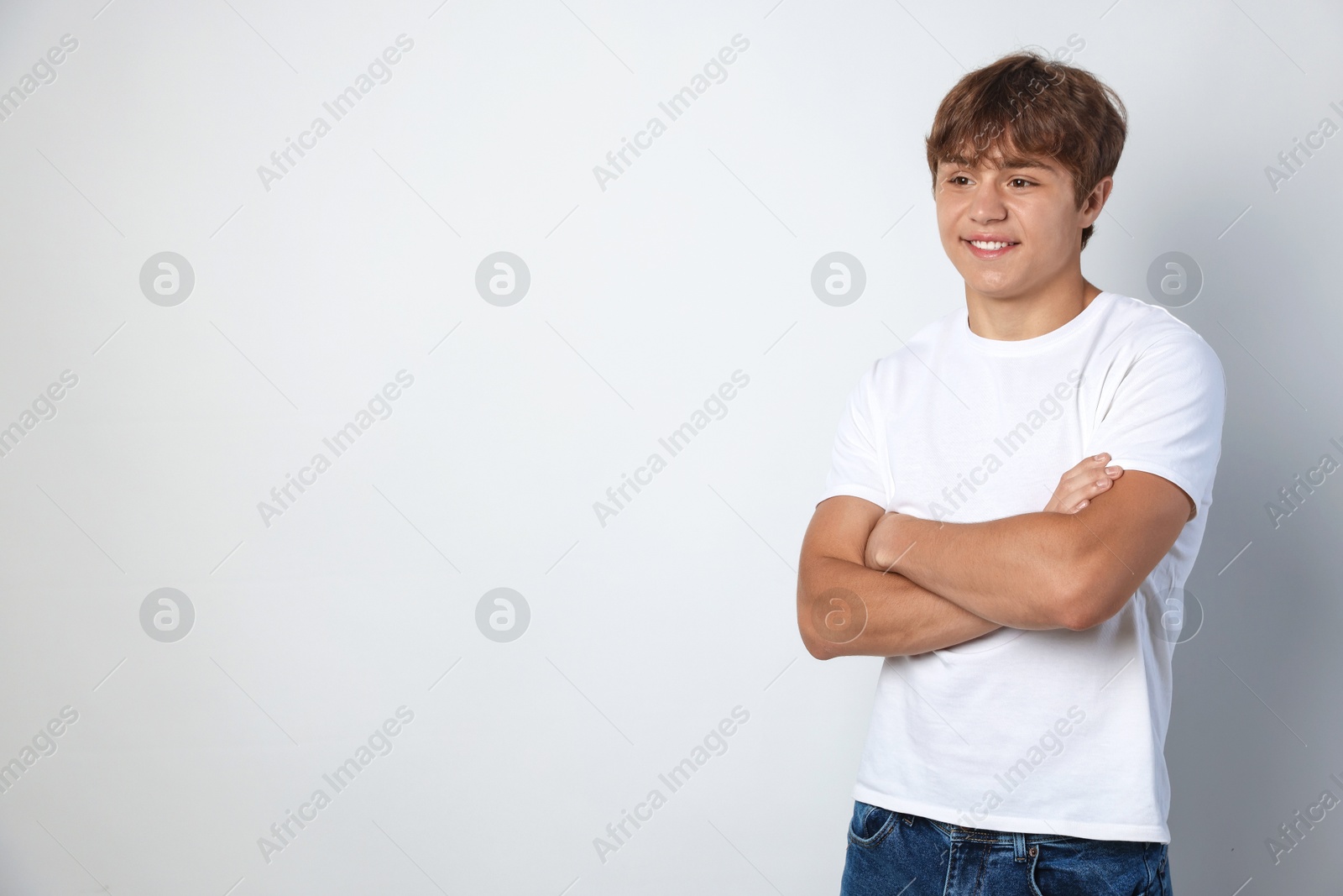 Photo of Smiling teenage boy with crossed arms on light grey background. Space for text