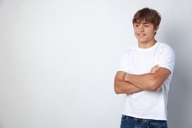 Photo of Smiling teenage boy with crossed arms on light grey background. Space for text