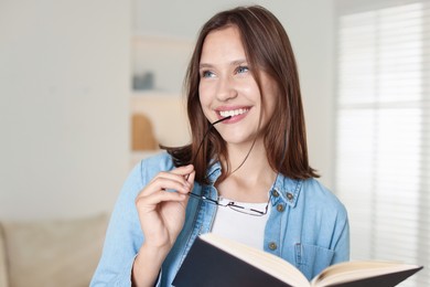 Photo of Smiling teenage girl with glasses and book at home