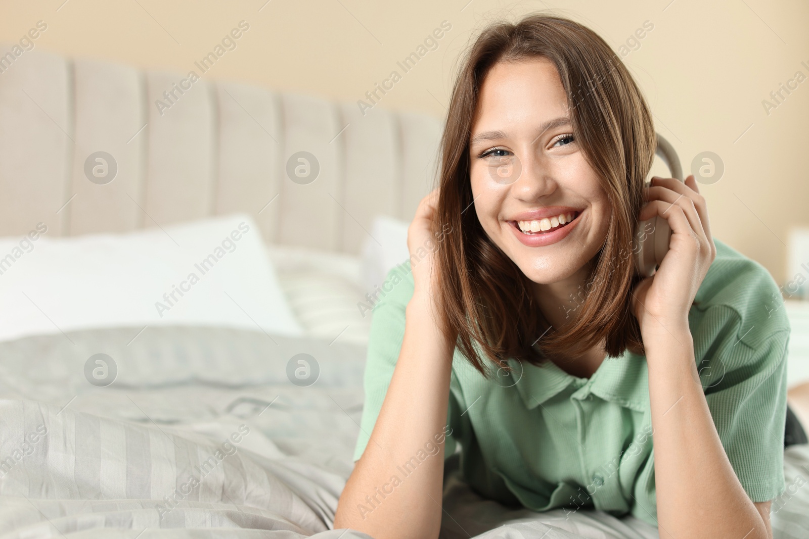 Smiling teenage girl with headphones on bed at home. Space for text Photo of Smiling teenage girl with headphones on bed at home. Space for text