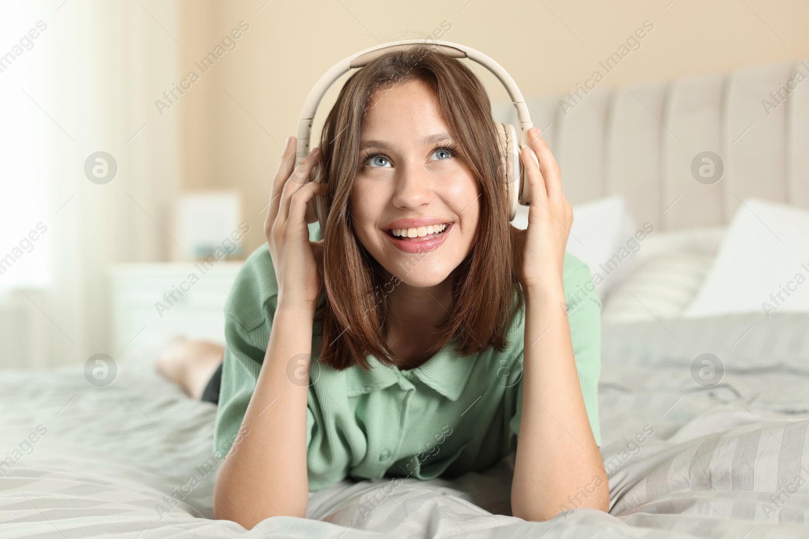 Smiling teenage girl in headphones listening to music on bed at home Photo of Smiling teenage girl in headphones listening to music on bed at home