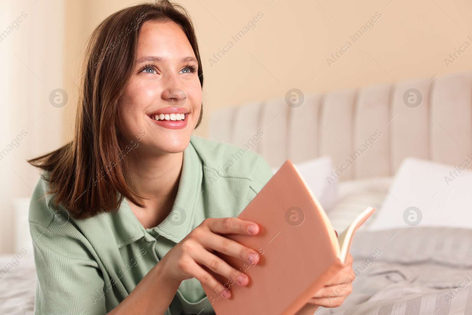 Smiling teenage girl with book on bed at home Photo of Smiling teenage girl with book on bed at home