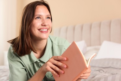 Photo of Smiling teenage girl with book on bed at home