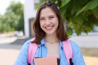 Photo of Portrait of smiling teenage girl with notebooks outdoors