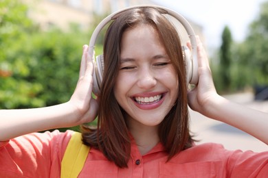 Photo of Smiling teenage girl in headphones listening to music outdoors, closeup