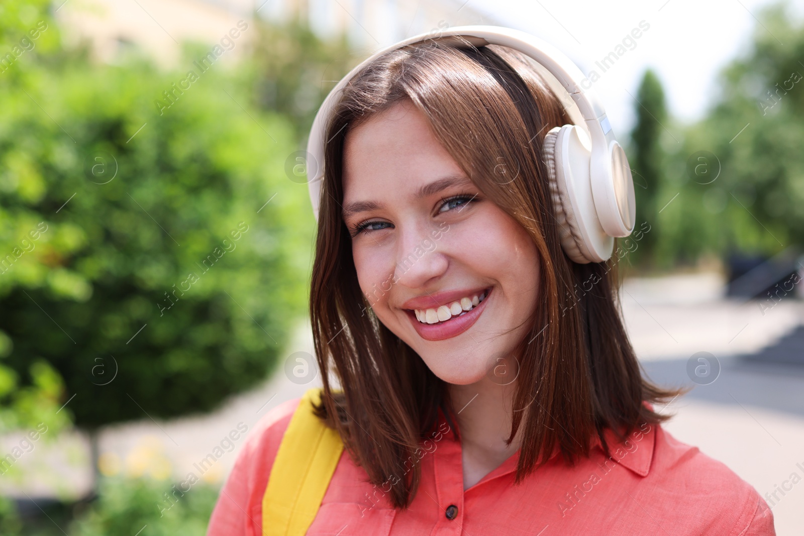 Photo of Smiling teenage girl in headphones listening to music outdoors