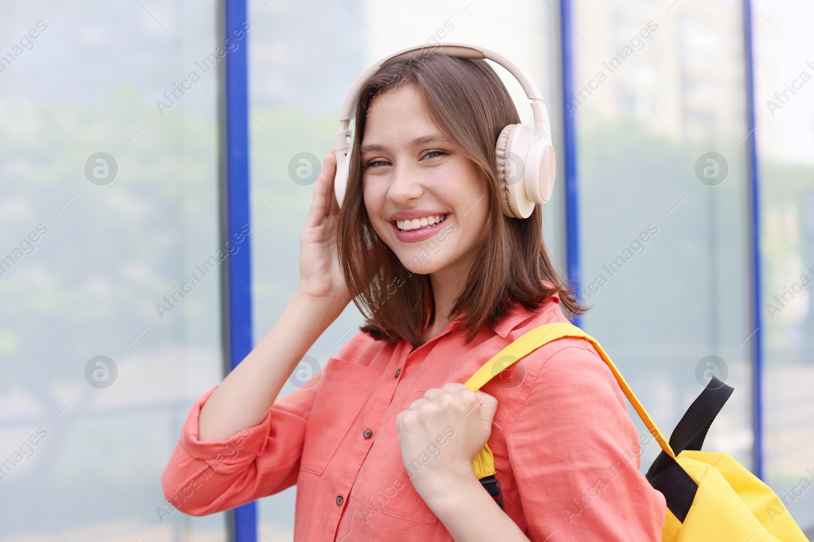 Smiling teenage girl in headphones listening to music near building outdoors Photo of Smiling teenage girl in headphones listening to music near building outdoors