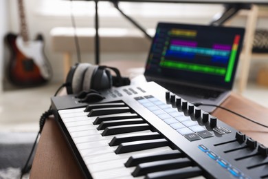 Photo of MIDI keyboard, laptop and headphones on wooden table in home studio, selective focus