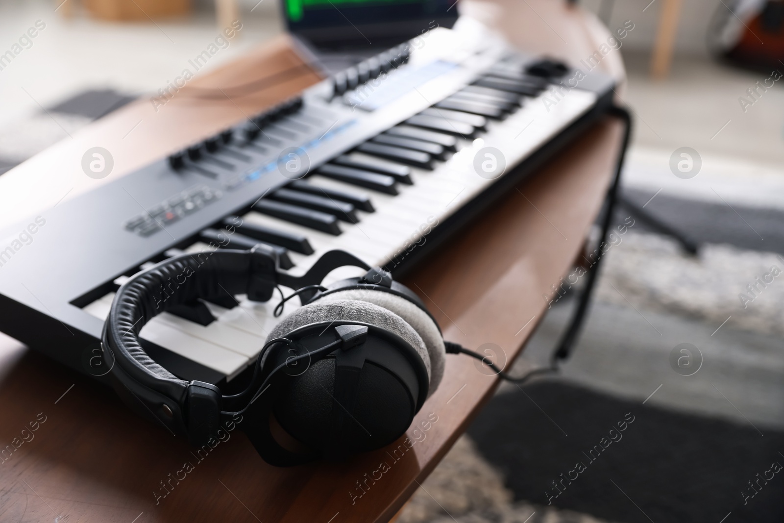 Photo of Headphones and MIDI keyboard on wooden table indoors, selective focus
