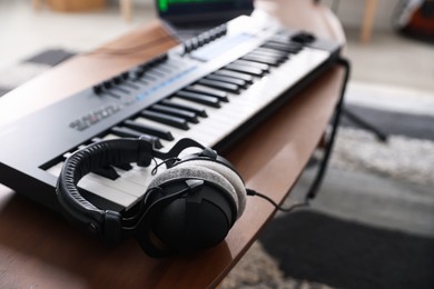 Photo of Headphones and MIDI keyboard on wooden table indoors, selective focus