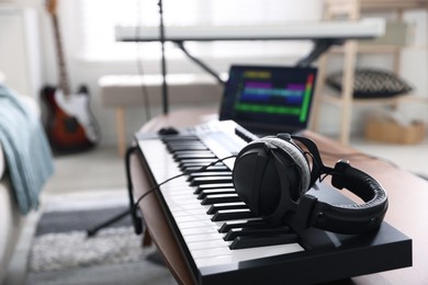 Photo of MIDI keyboard, laptop and headphones on wooden table in home studio, selective focus