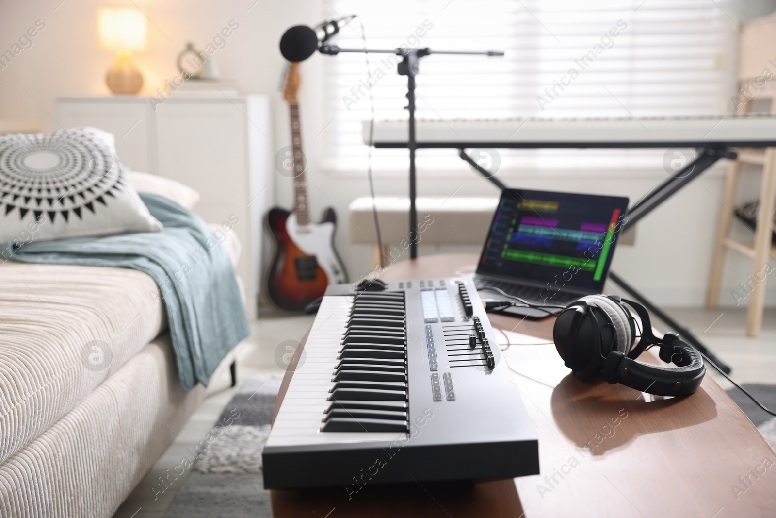 Photo of MIDI keyboard, laptop and headphones on wooden table in home studio