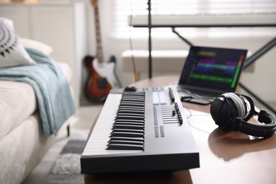 Photo of MIDI keyboard, laptop and headphones on wooden table in home studio, selective focus