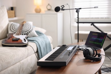 Photo of MIDI keyboard, laptop and headphones on wooden table in home studio