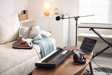 Photo of MIDI keyboard, laptop and headphones on wooden table in home studio