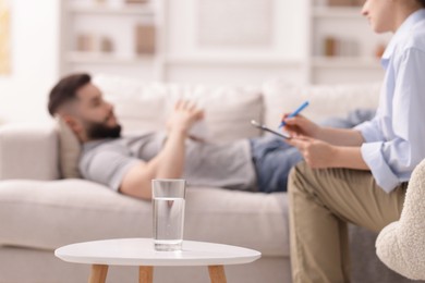 Photo of Professional psychologist working with patient in office, focus on glass of water