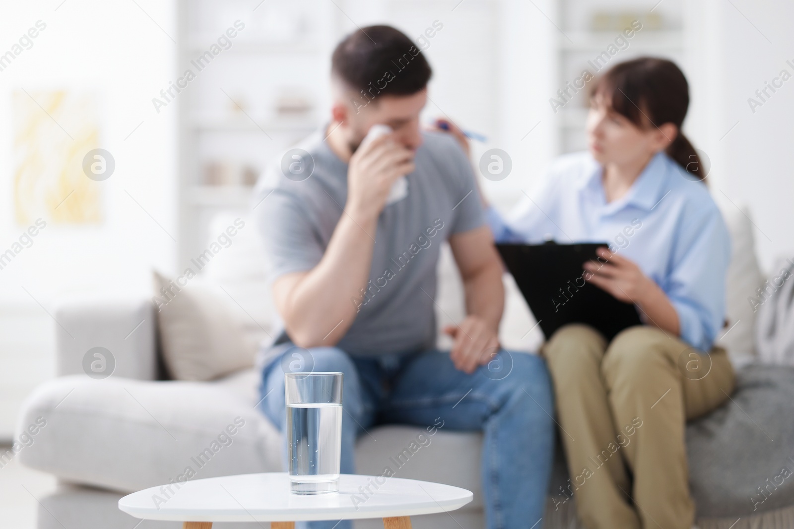 Photo of Psychologist supporting patient during therapy session in office, focus on glass of water
