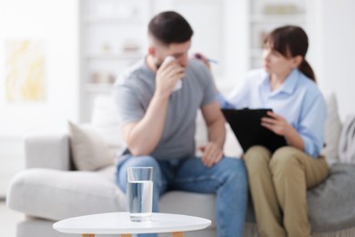 Photo of Psychologist supporting patient during therapy session in office, focus on glass of water