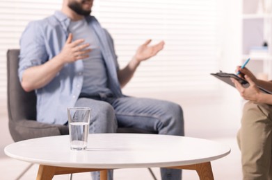 Photo of Professional psychologist working with patient in office, focus on glass of water