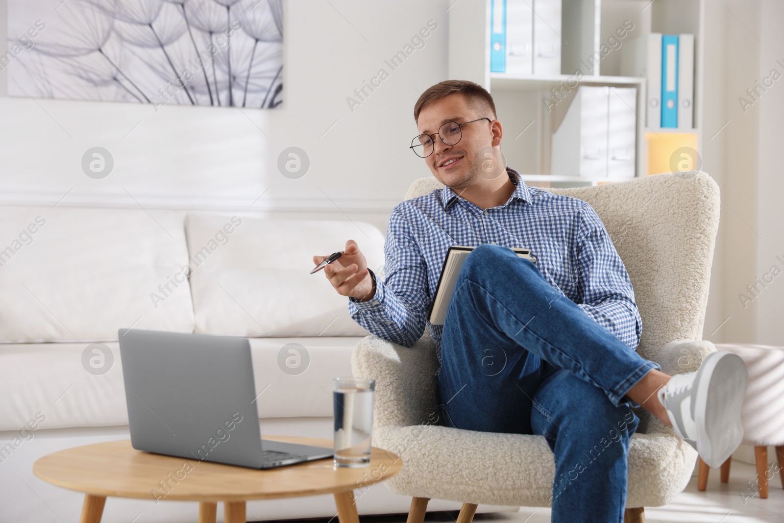 Photo of Smiling psychologist in glasses with notepad during online session by laptop in office