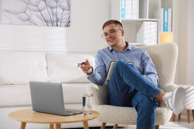 Photo of Smiling psychologist in glasses with notepad during online session by laptop in office