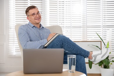 Photo of Smiling psychologist in glasses with notepad during online session by laptop in office