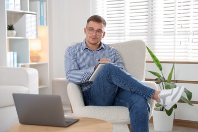 Photo of Psychologist in glasses with notepad during online session by laptop in office
