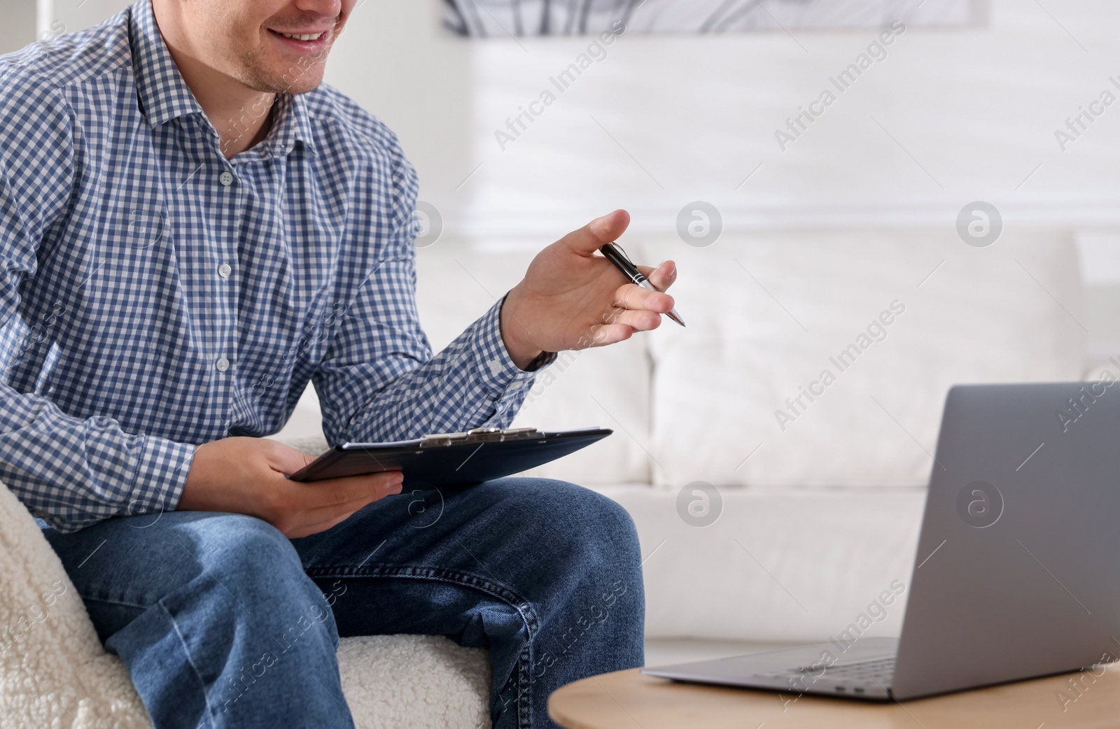 Photo of Smiling psychologist with clipboard and pen during online session by laptop in office, closeup