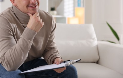 Photo of Smiling psychologist with clipboard and pen on sofa in office, closeup. Space for text