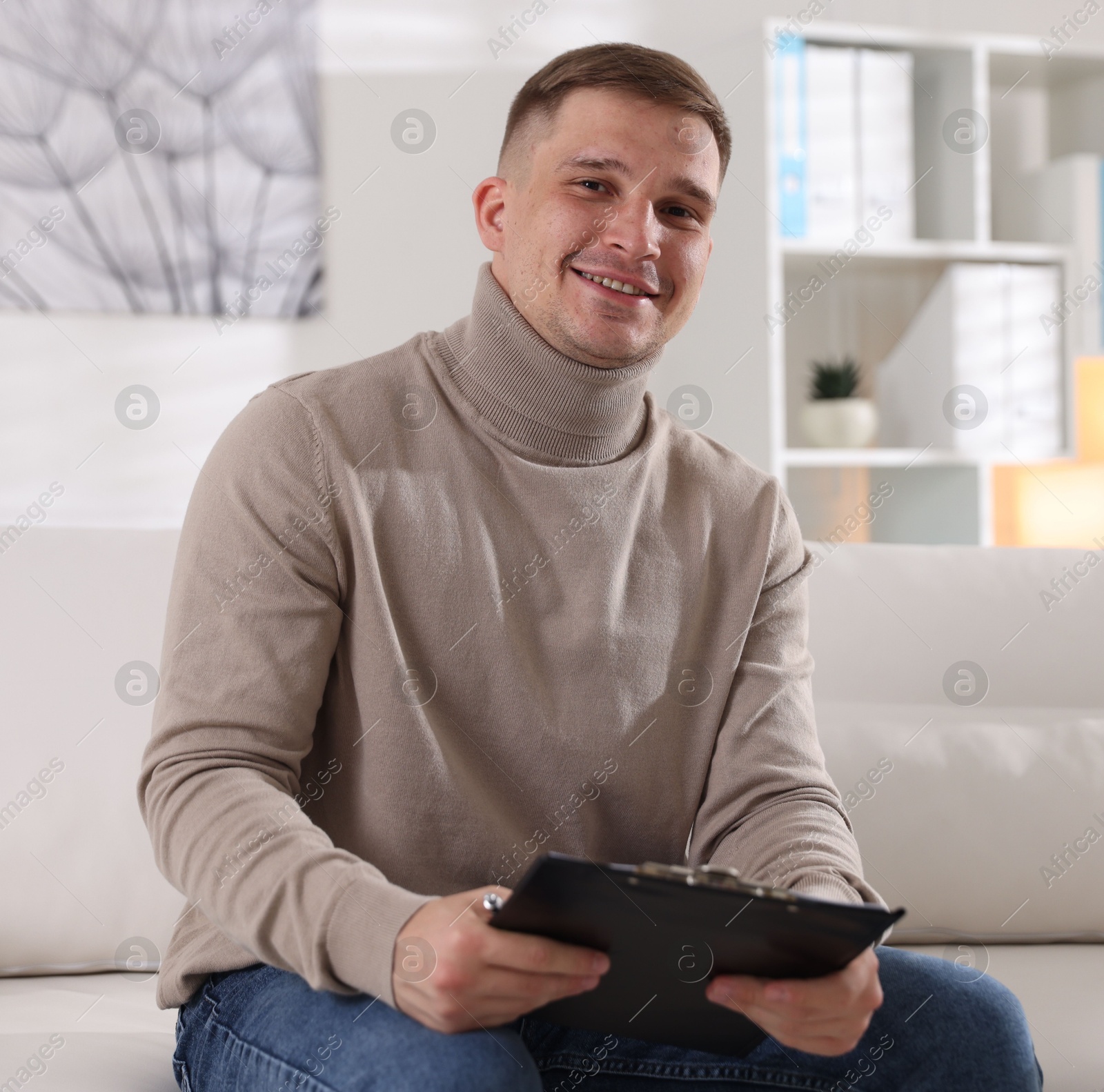 Photo of Portrait of smiling psychologist with clipboard on sofa in office
