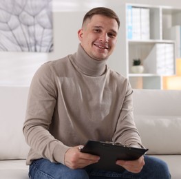 Photo of Portrait of smiling psychologist with clipboard on sofa in office