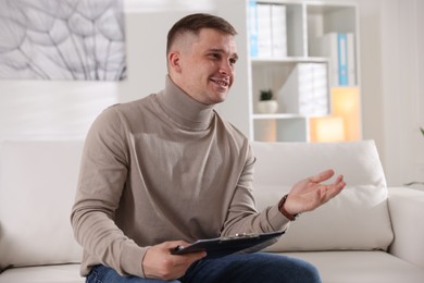 Photo of Smiling psychologist with clipboard on sofa in office