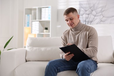 Photo of Smiling psychologist with clipboard on sofa in office