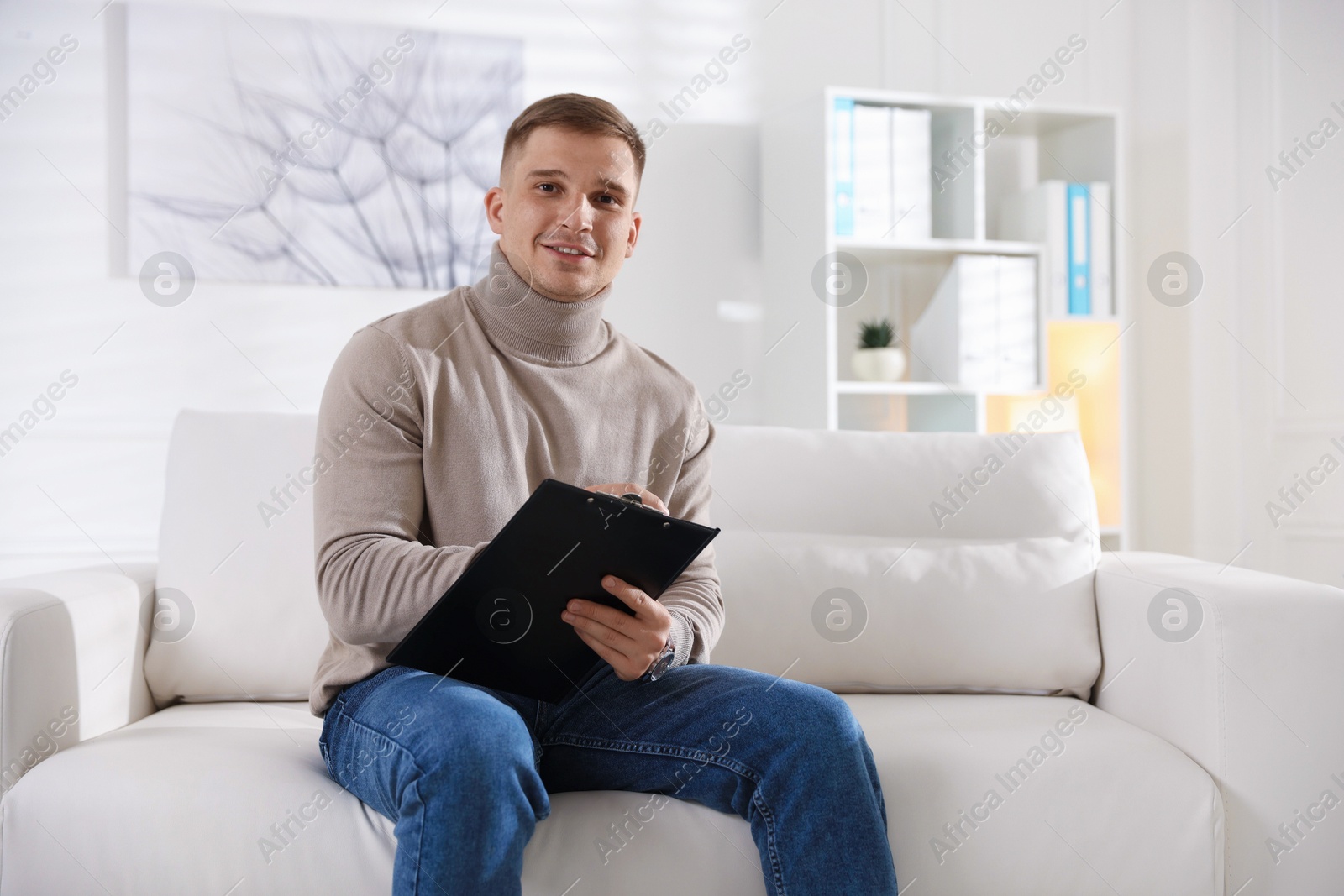Photo of Portrait of smiling psychologist with clipboard on sofa in office