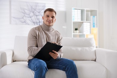 Photo of Portrait of smiling psychologist with clipboard on sofa in office