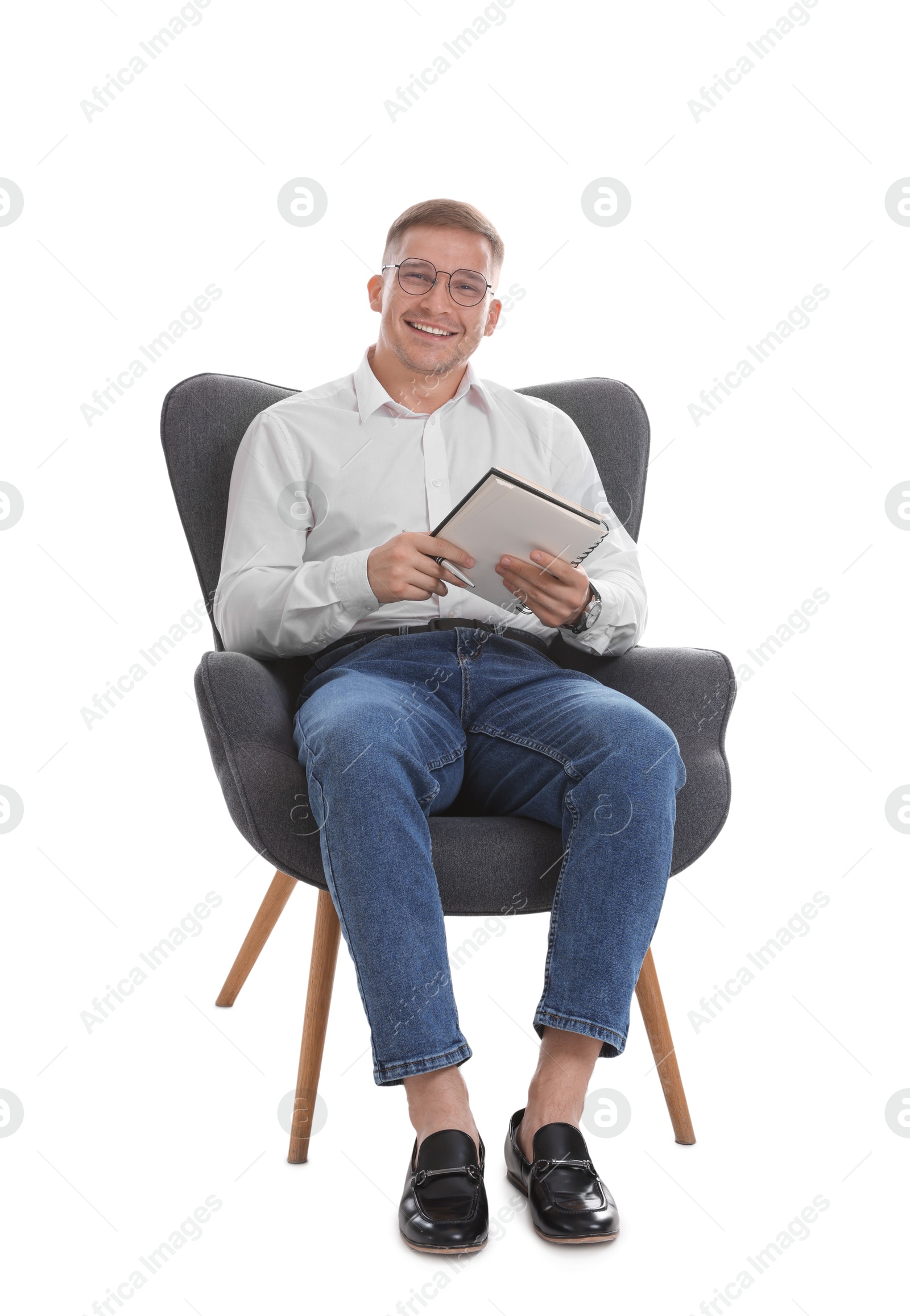 Photo of Smiling psychologist in glasses with notepad sitting on armchair against white background