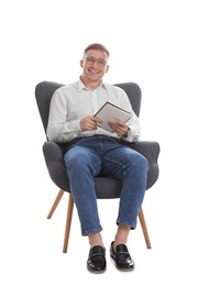 Photo of Smiling psychologist in glasses with notepad sitting on armchair against white background