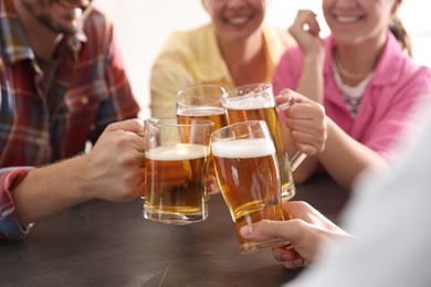 Photo of Friends clinking glasses of beer at grey table indoors, closeup