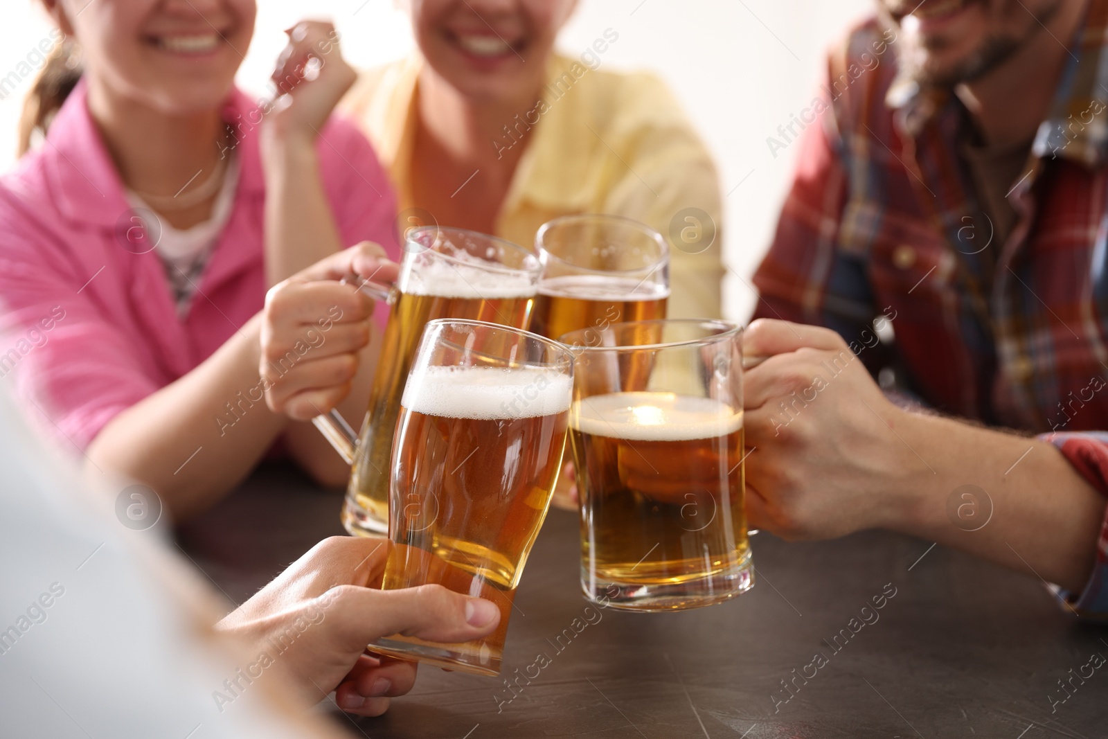 Photo of Friends clinking glasses of beer at grey table indoors, closeup