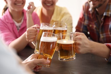 Photo of Friends clinking glasses of beer at grey table indoors, closeup
