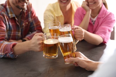 Photo of Friends clinking glasses of beer at grey table indoors, closeup